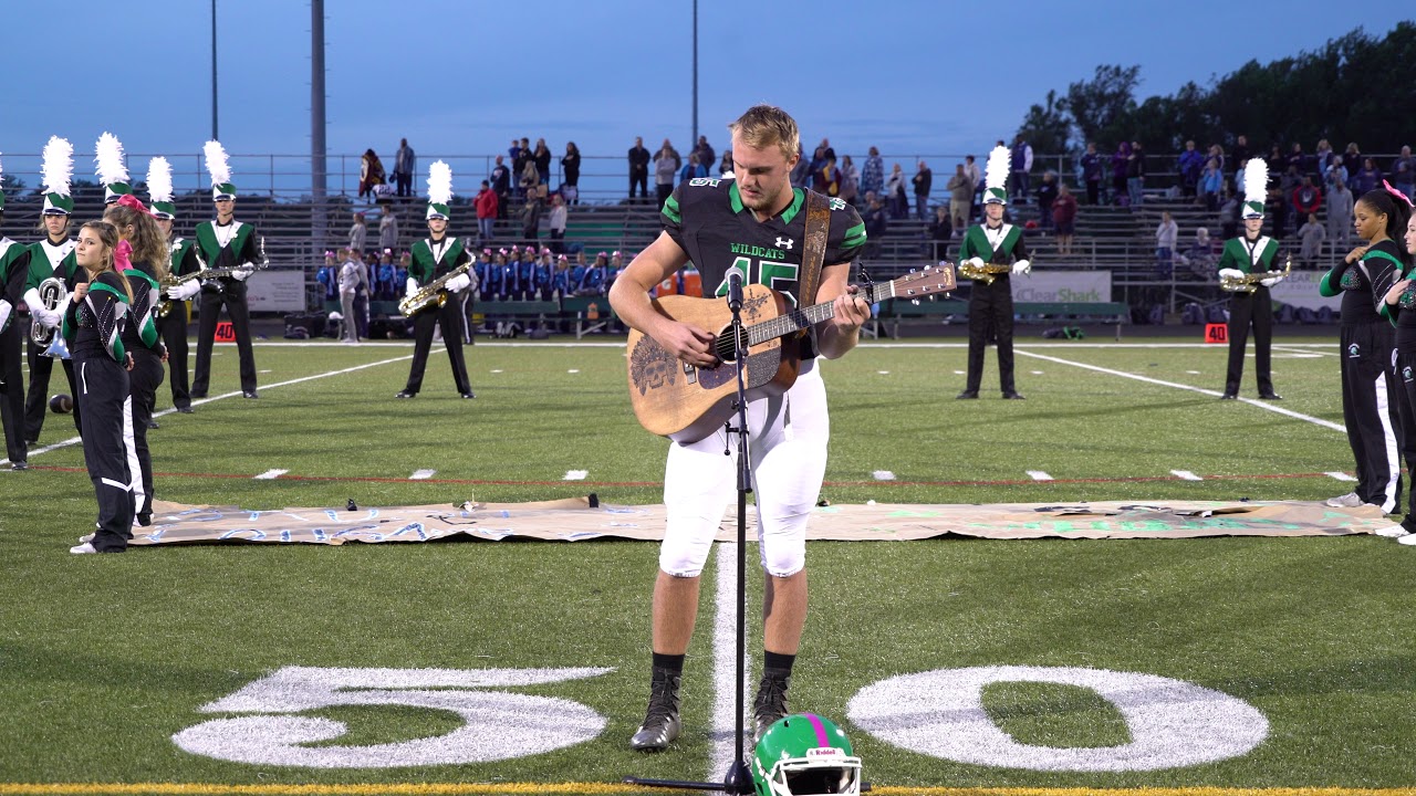 American high school football player plays the national anthem on the field with guitar